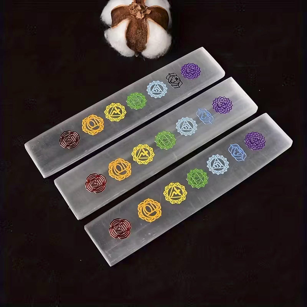 Three rectangular white Moroccan selenite charging bars engraved with colorful seven chakra symbols on a black background.