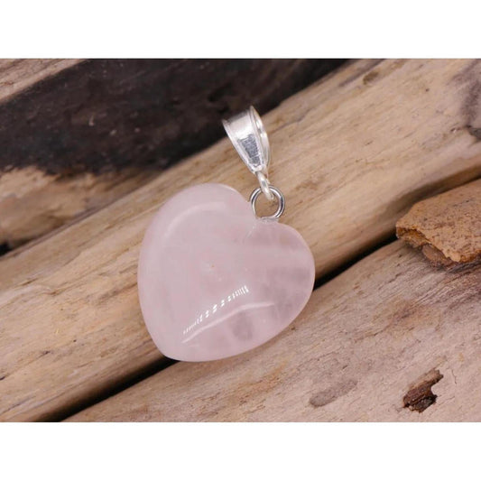 Hand-carved pale pink rose quartz heart pendant with a silver bail, resting on a textured wooden surface.