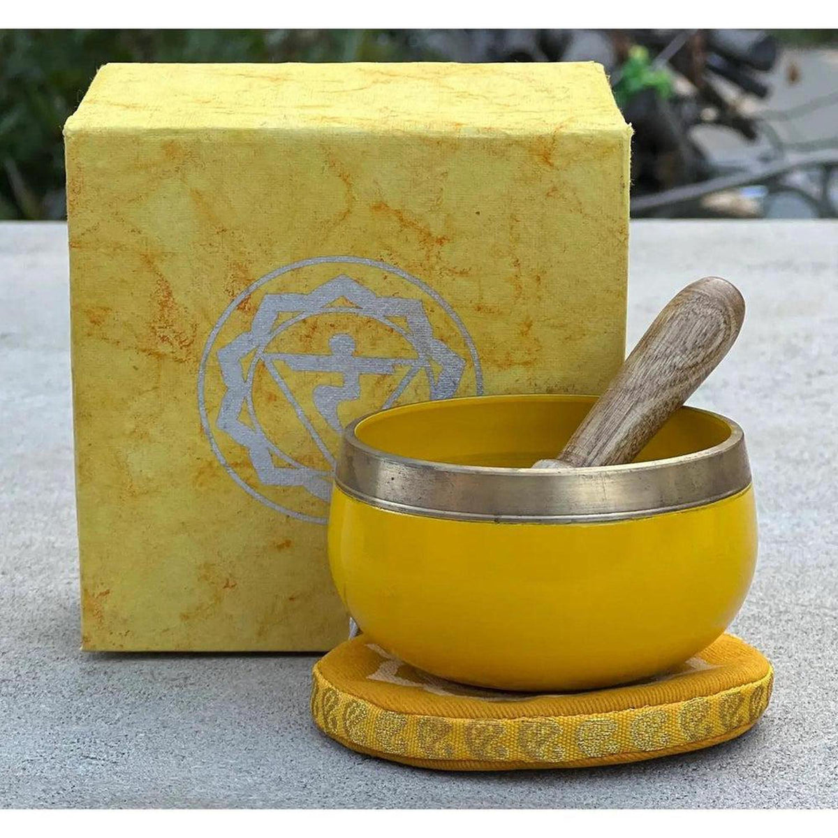 Yellow brass singing bowl with wooden striker, matching yellow cushion, and gift box featuring the Solar Plexus symbol.