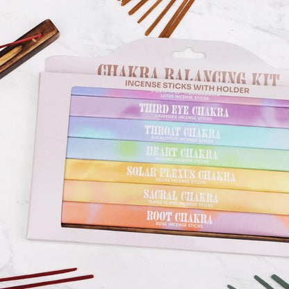 7 Chakra incense gift set with colorful boxes, wooden holder, and bamboo sticks on a white marble background.