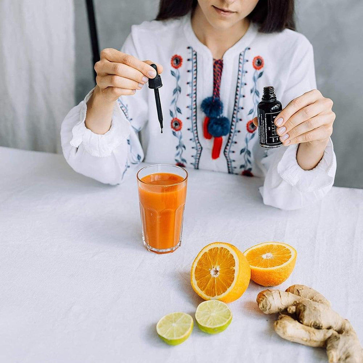 Woman adding Black Diamond Shilajit liquid drops from a 50ml glass bottle into a glass of orange juice with fresh citrus and ginger.