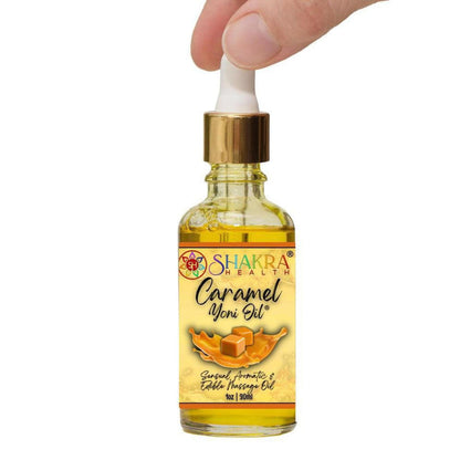 Small glass dropper bottle of Shakra Health caramel yoni oil with a gold cap, held by fingers against a white background.