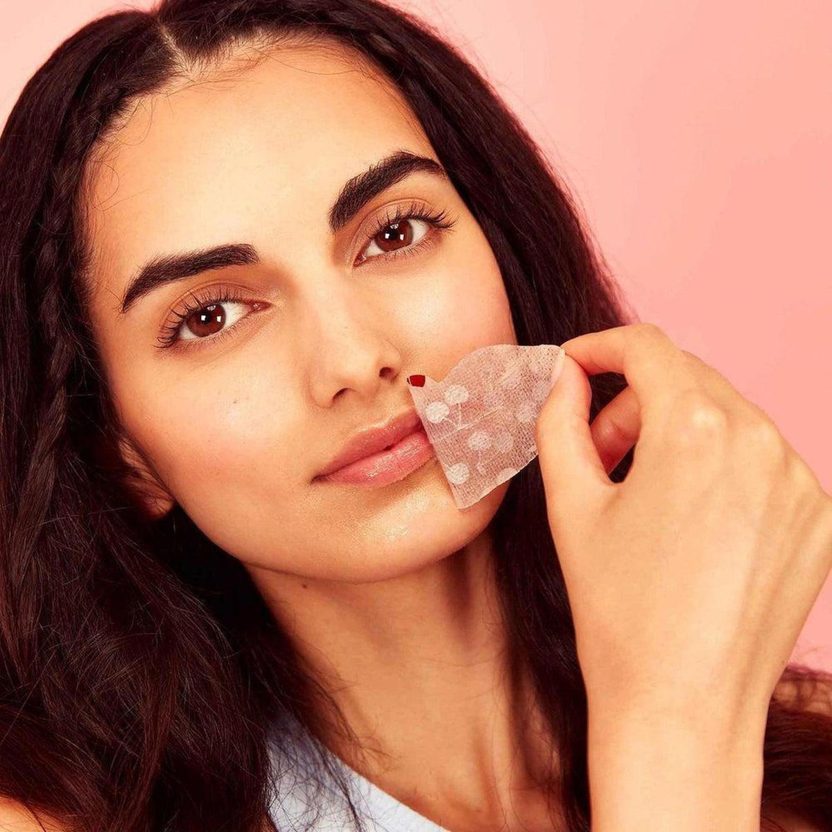 Woman applying a translucent hydrogel lip mask with a delicate cherry pattern against a soft pink background.