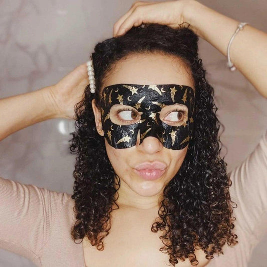 Woman wearing a black hydrogel goggle eye mask with gold star and moon patterns covering her upper face.