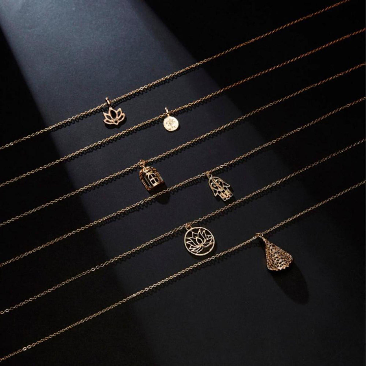 Six delicate gold-tone chain necklaces featuring spiritual pendants like the lotus, hamsa hand, and cage charms.