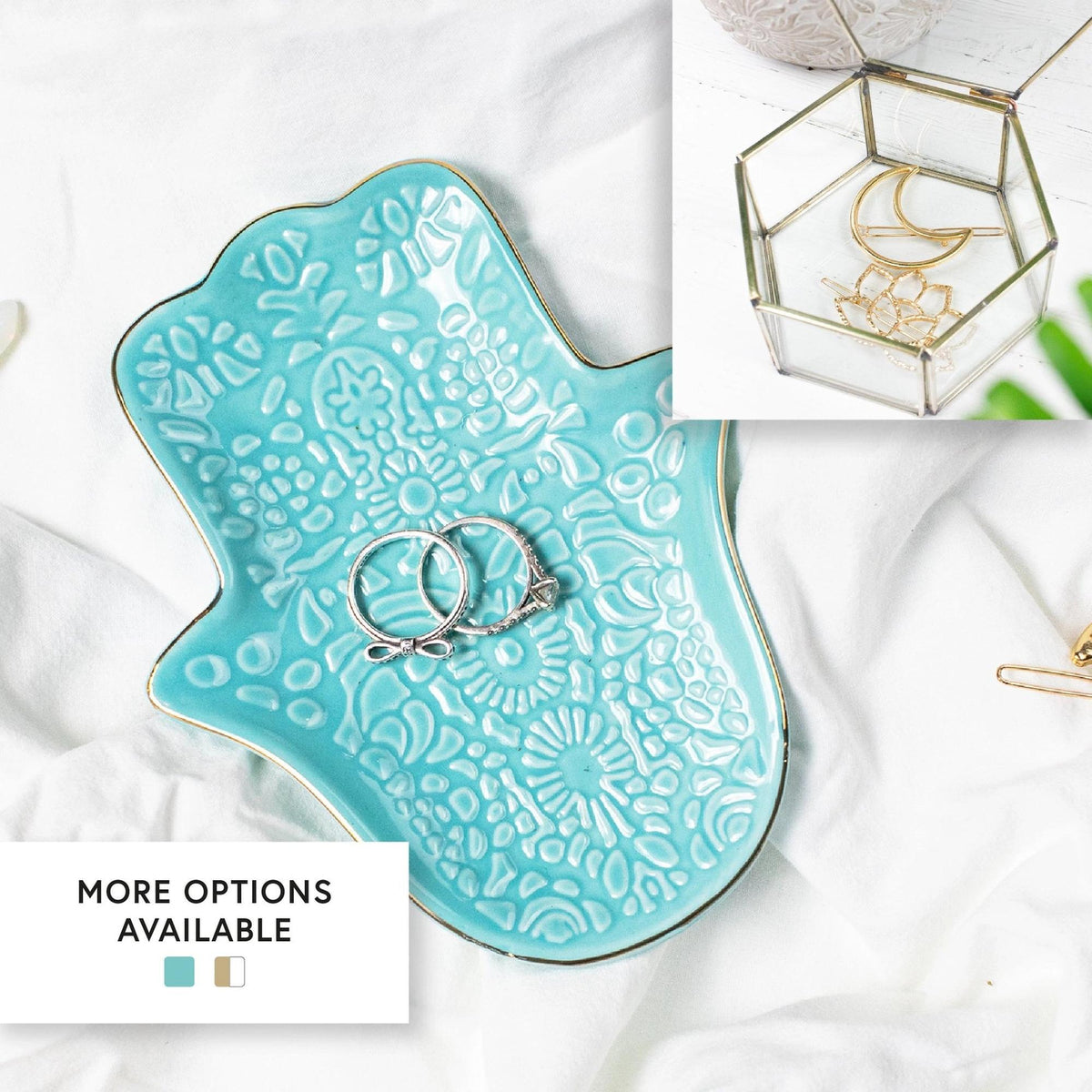Turquoise ceramic Hamsa hand jewellery dish with gold trim, holding silver rings on a white fabric background.