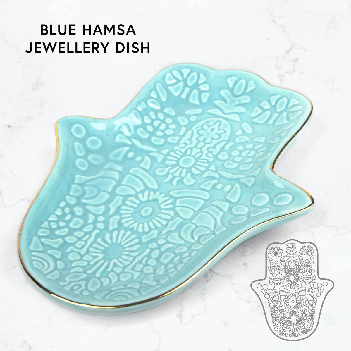 Light blue ceramic Hamsa hand jewellery dish with intricate embossed patterns and a gold-trimmed edge on a marble surface.