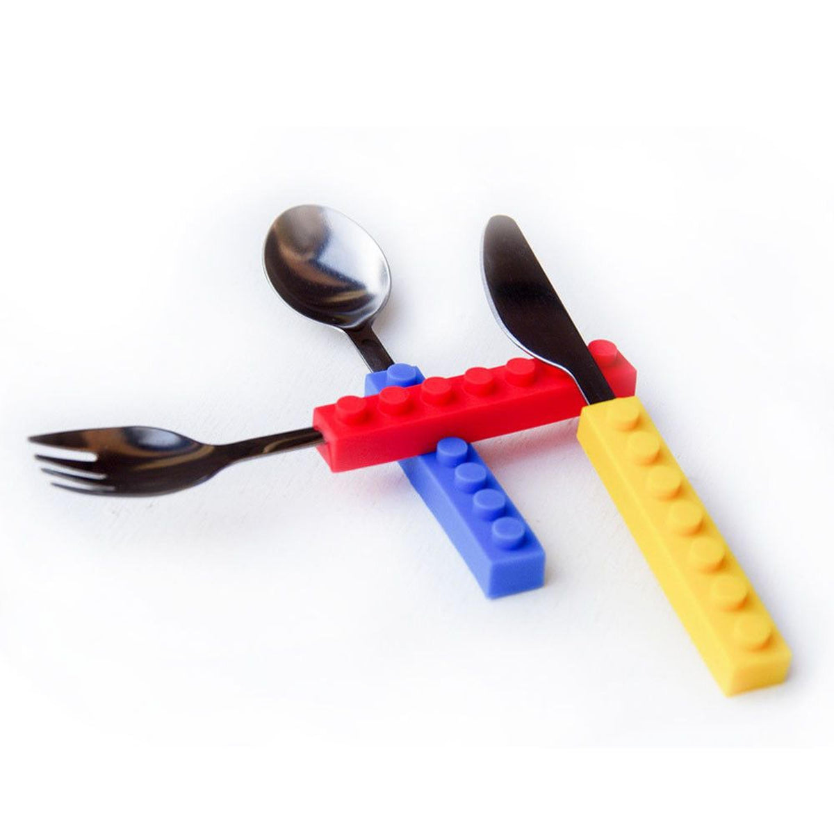 Three-piece stainless steel kids' cutlery set with interlocking red, blue, and yellow silicone building block handles.