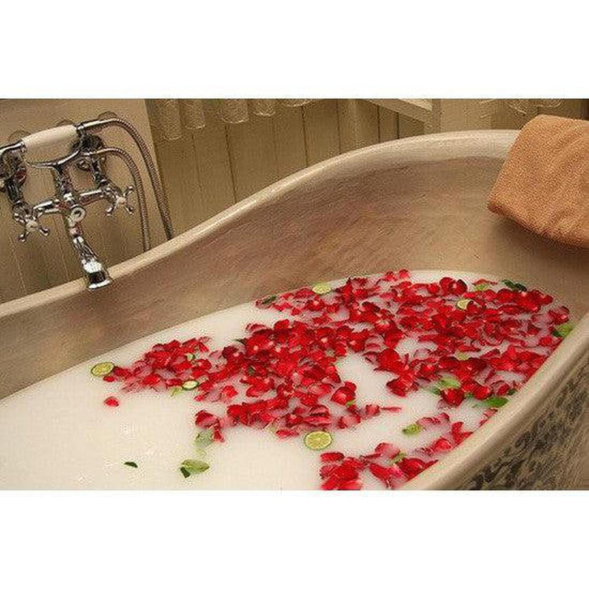 Bathtub filled with milky water, scattered red soap rose petals, and lime slices for a luxurious spa experience.