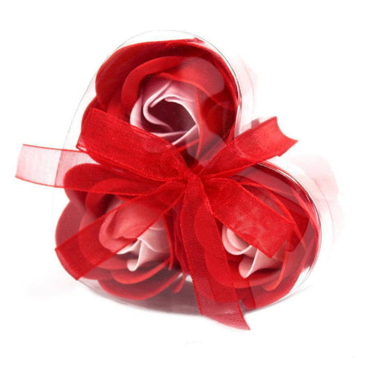 Three red soap roses in a heart-shaped clear gift box tied with a decorative red ribbon on a white background.