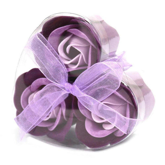 Three purple soap roses in a heart-shaped gift box, tied with a matching sheer lavender ribbon.