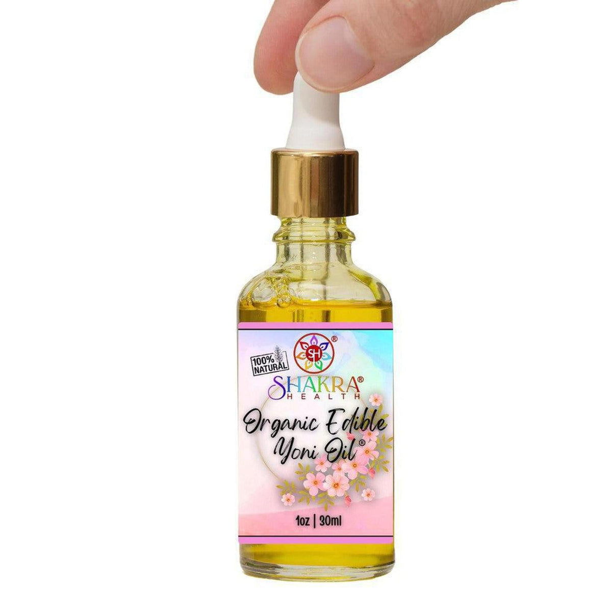 Hand held 30ml glass dropper bottle of Shakra Health organic edible yoni oil with a floral label against a white background.