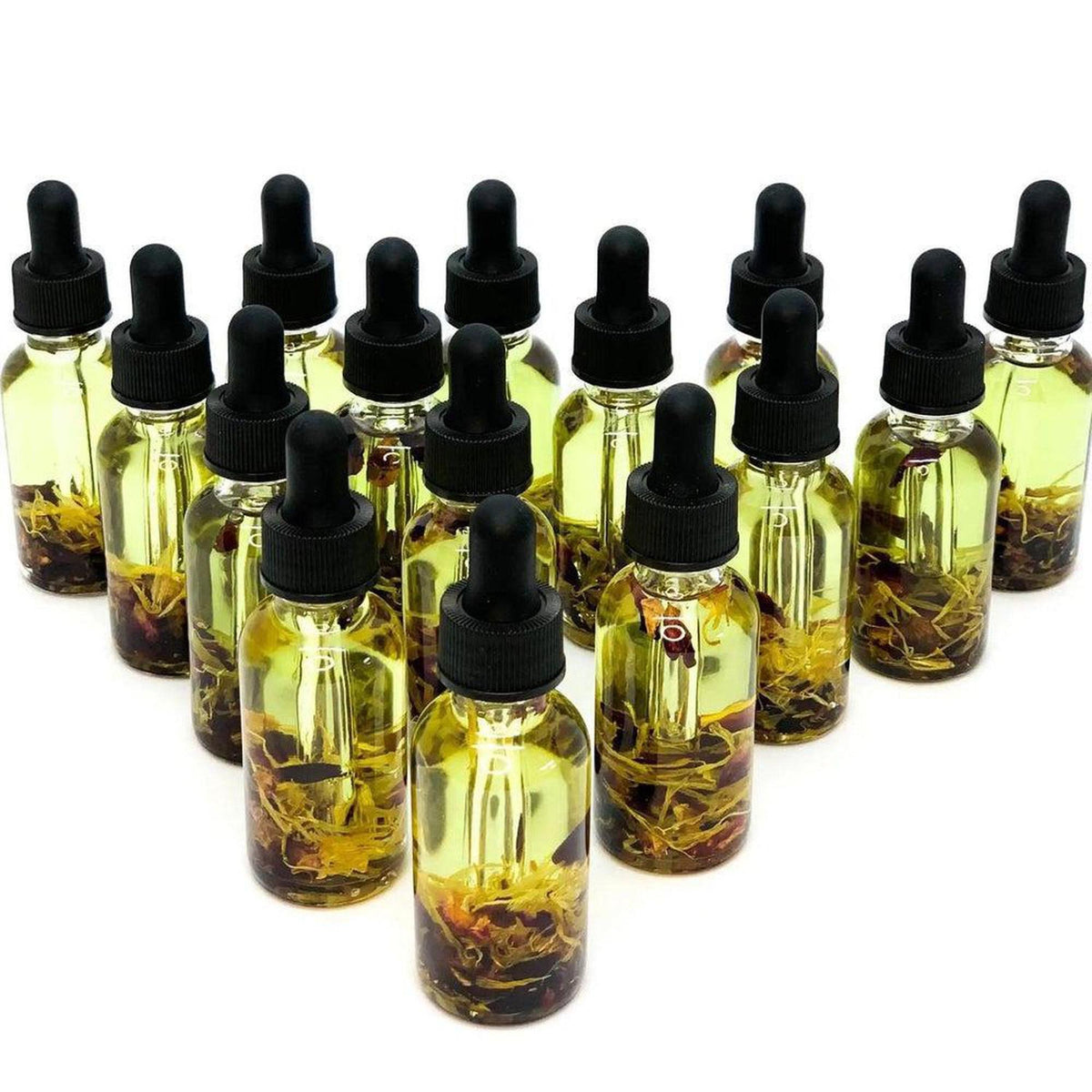 Group of small glass dropper bottles filled with golden botanical yoni oil and dried flower petals on a white background.