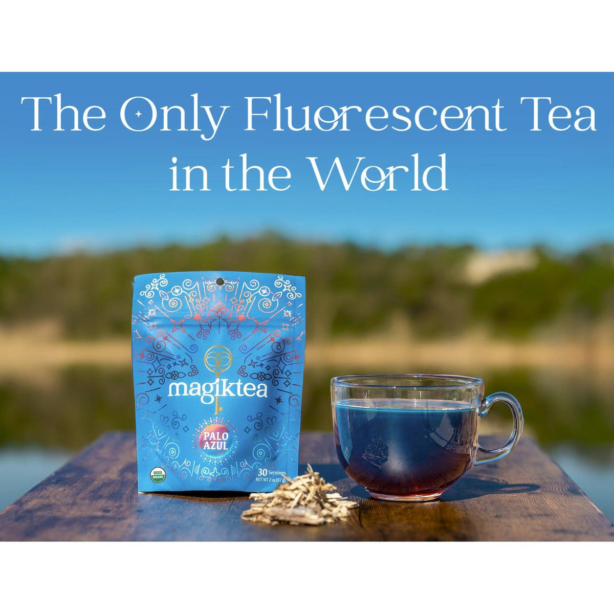Magiktea Palo Azul pouch with a glass of fluorescent blue herbal tea on a wooden surface against a blurred outdoor background.