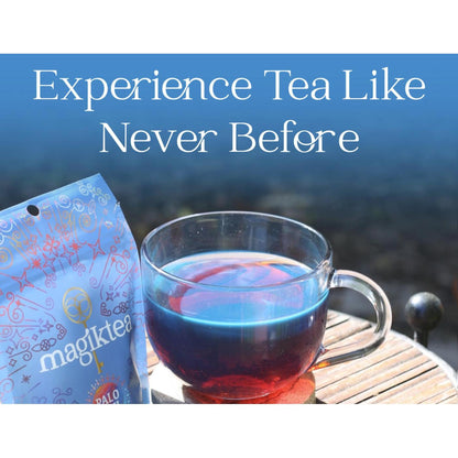 Magiktea Palo Azul pouch next to a glass cup filled with glowing, fluorescent blue herbal tea on a wooden table.