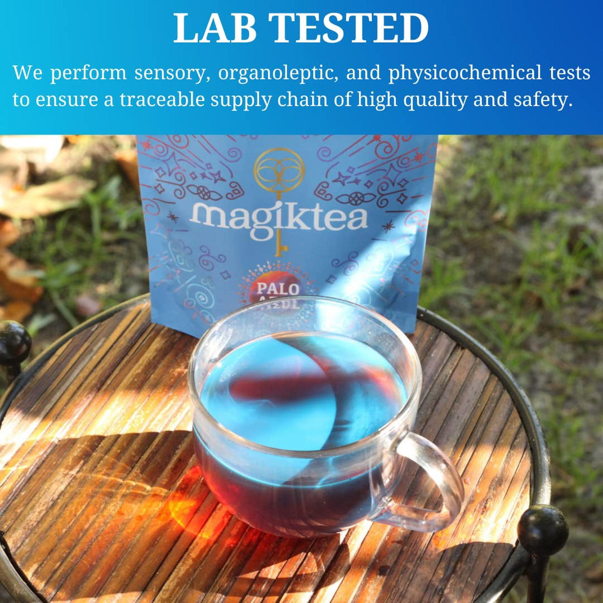 Glass mug filled with fluorescent blue Palo Azul tea sitting on a small wooden table in front of a Magiktea pouch.
