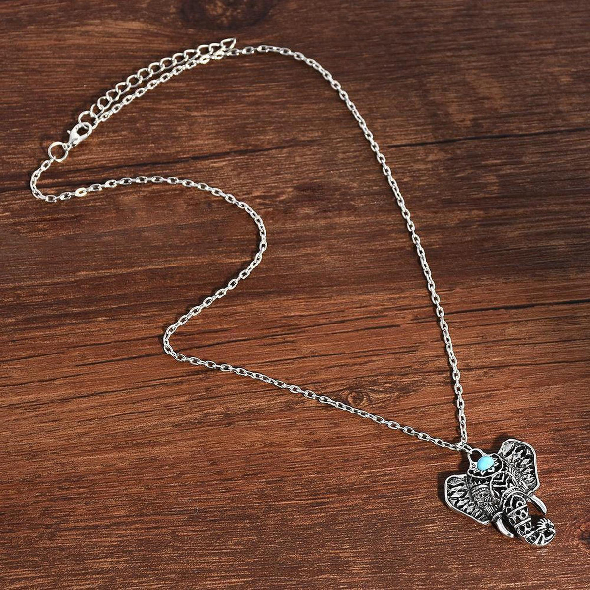 Antique silver-plated elephant pendant necklace with a small blue stone accent on a delicate chain against a wood background.