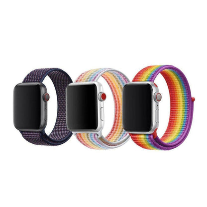 Three Apple Watches with adjustable nylon loop straps in dark blue, pastel rainbow, and vibrant rainbow patterns.