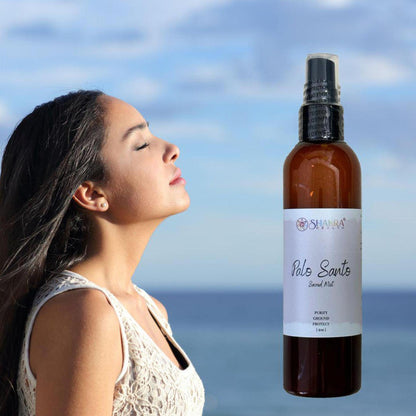 Amber glass spray bottle of Palo Santo Sacred Mist next to a woman with eyes closed against a blurred ocean background.