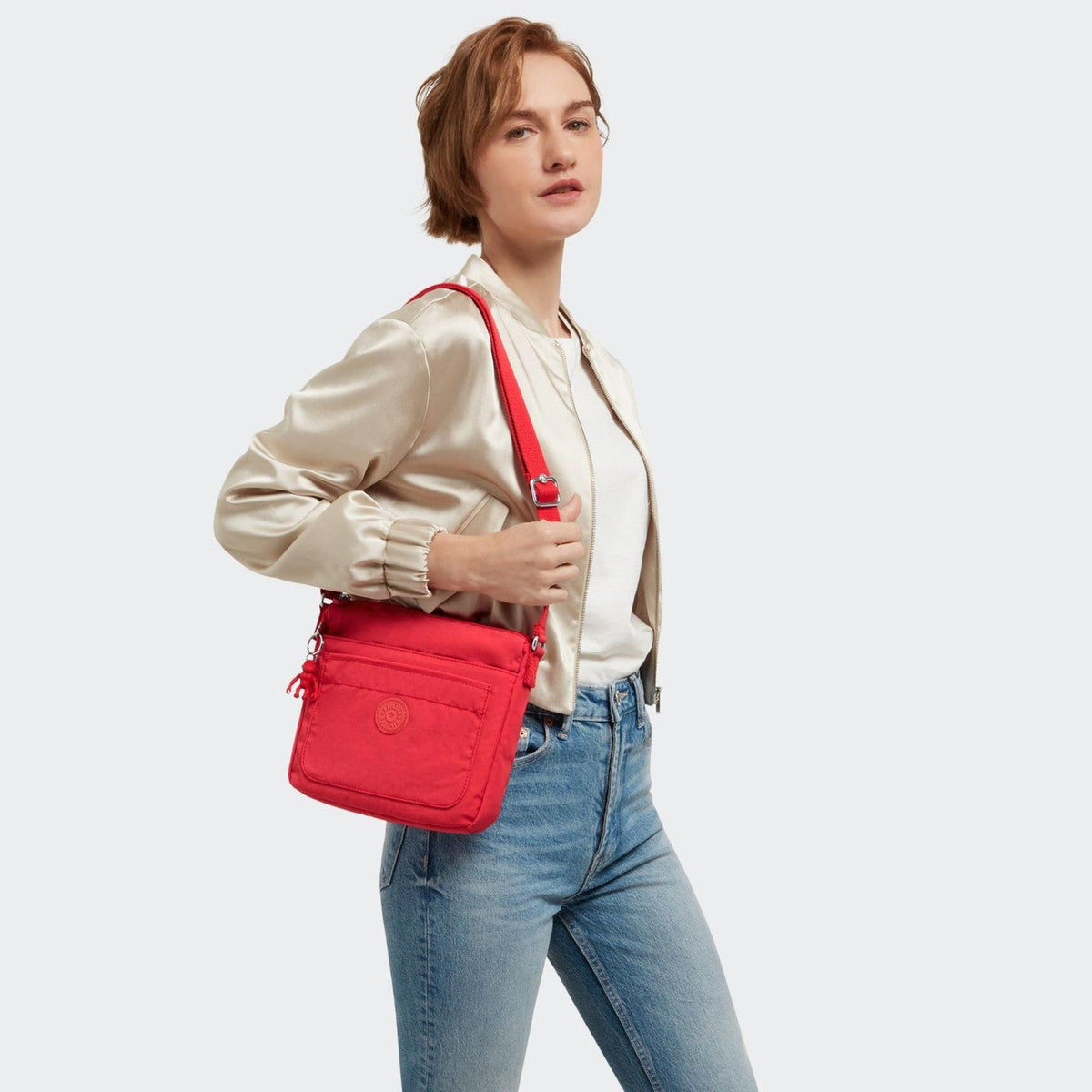 Woman wearing a vibrant party pink Kipling Sebastian medium crossbody bag with a front zip pocket and adjustable strap.