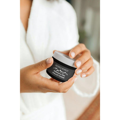 Person holding a small black jar of Sacred Remedy premium Himalayan Shilajit powder with a white lid.