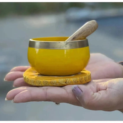 Handheld yellow brass singing bowl on a matching cushion with a wooden mallet for Solar Plexus chakra sound healing.