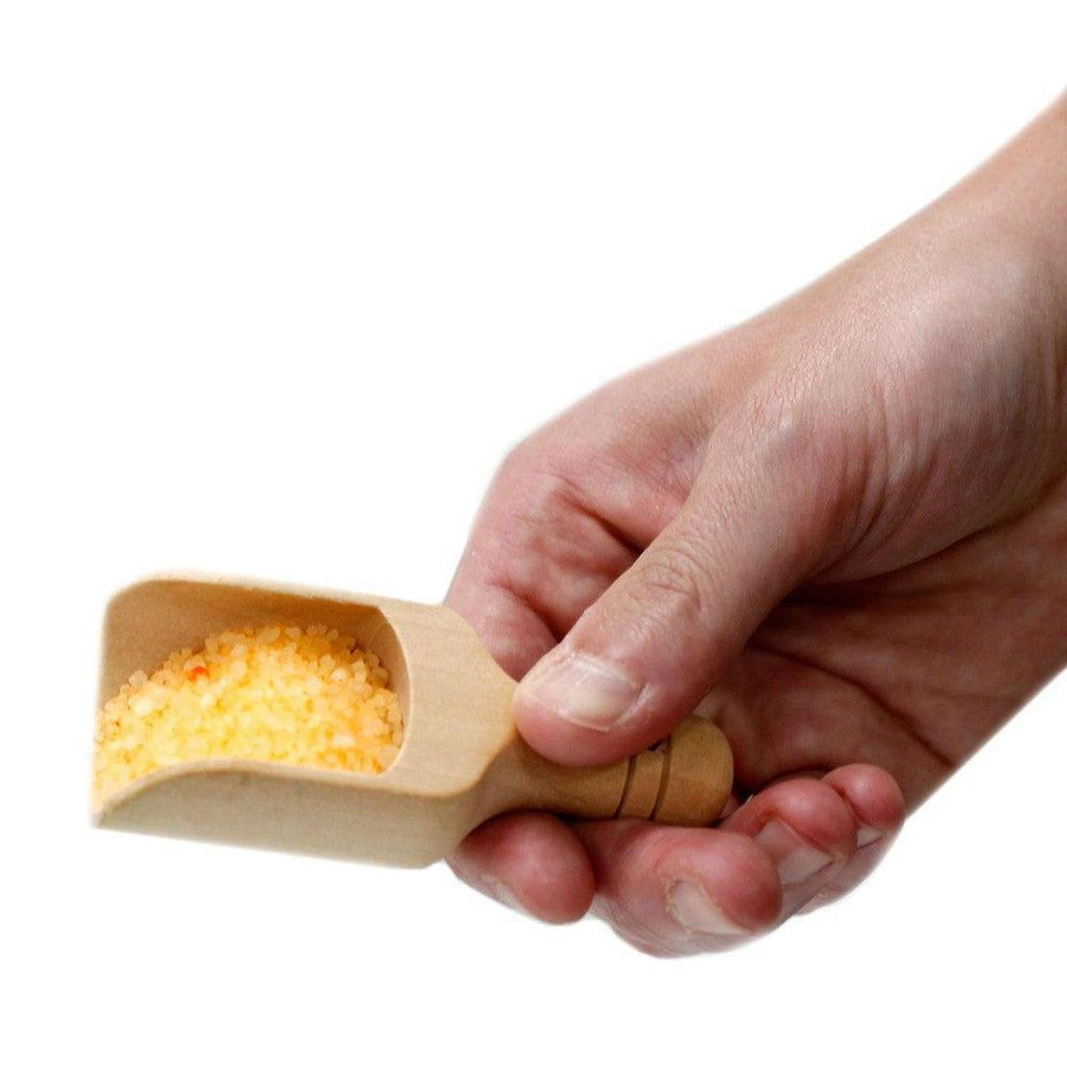 Hand holding a small wooden scoop filled with yellow Total Detox aromatherapy sea salt crystals.