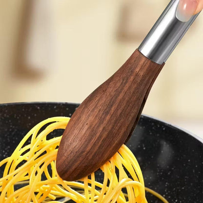 Kitchen tongs with natural walnut wood heads and stainless steel handles lifting spaghetti from a non-stick pan.