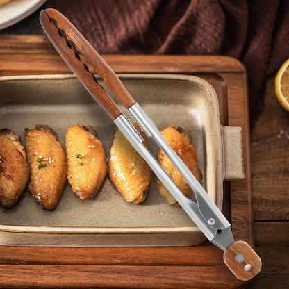 Stainless steel kitchen tongs with walnut wood heads and handle accents, shown serving roasted chicken wings.