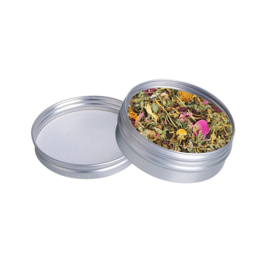 Organic yoni steam herbs with dried flowers in a small, round silver metal tin with a matching lid on a white background.